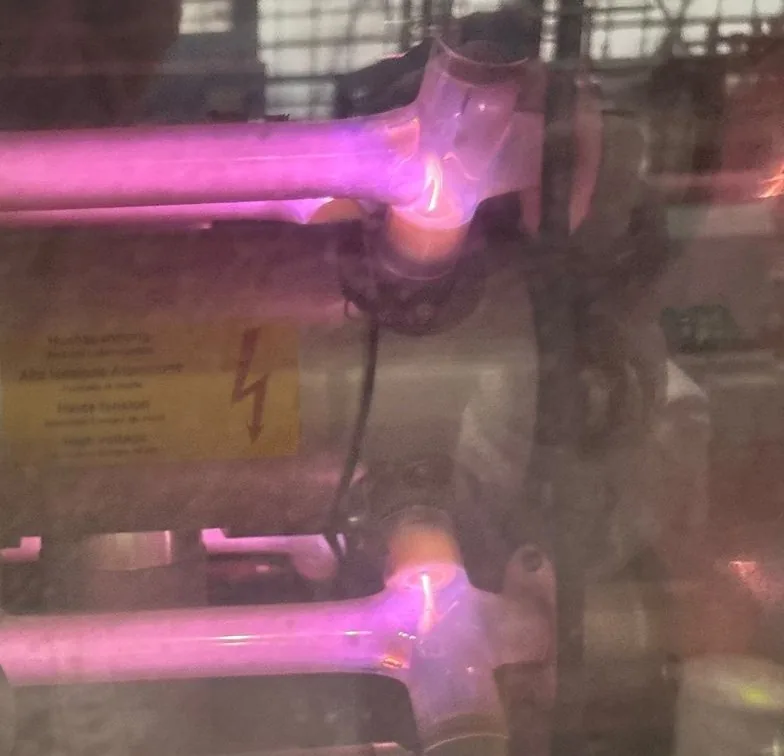 Magenta leuchtende Glasröhren eines CO2-Lasers hinter einer Scheibe