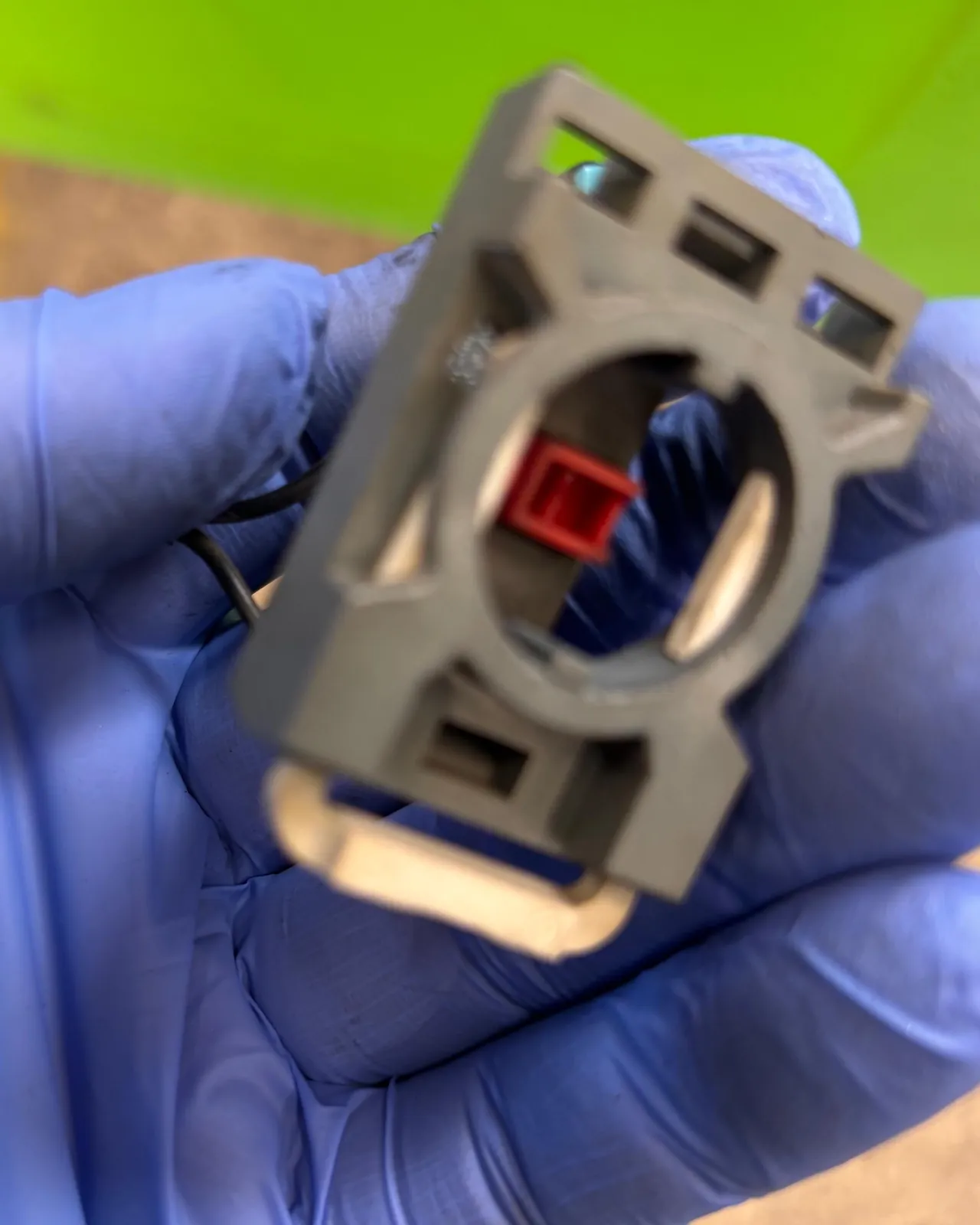 Grauer Hilfsschalterblock mit rotem Stößel in einer Hand mit blauem Handschuh