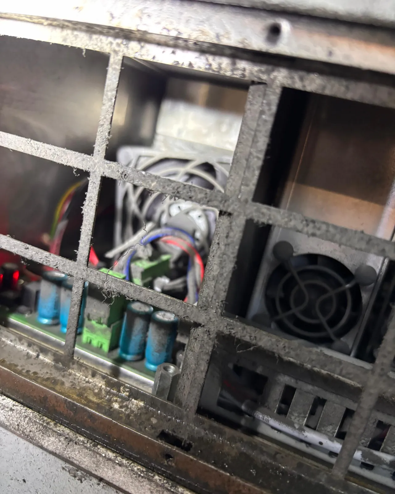 Stark verstaubtes Lüftungsgitter vor einer Netzteilplatine und einem Lüfter
