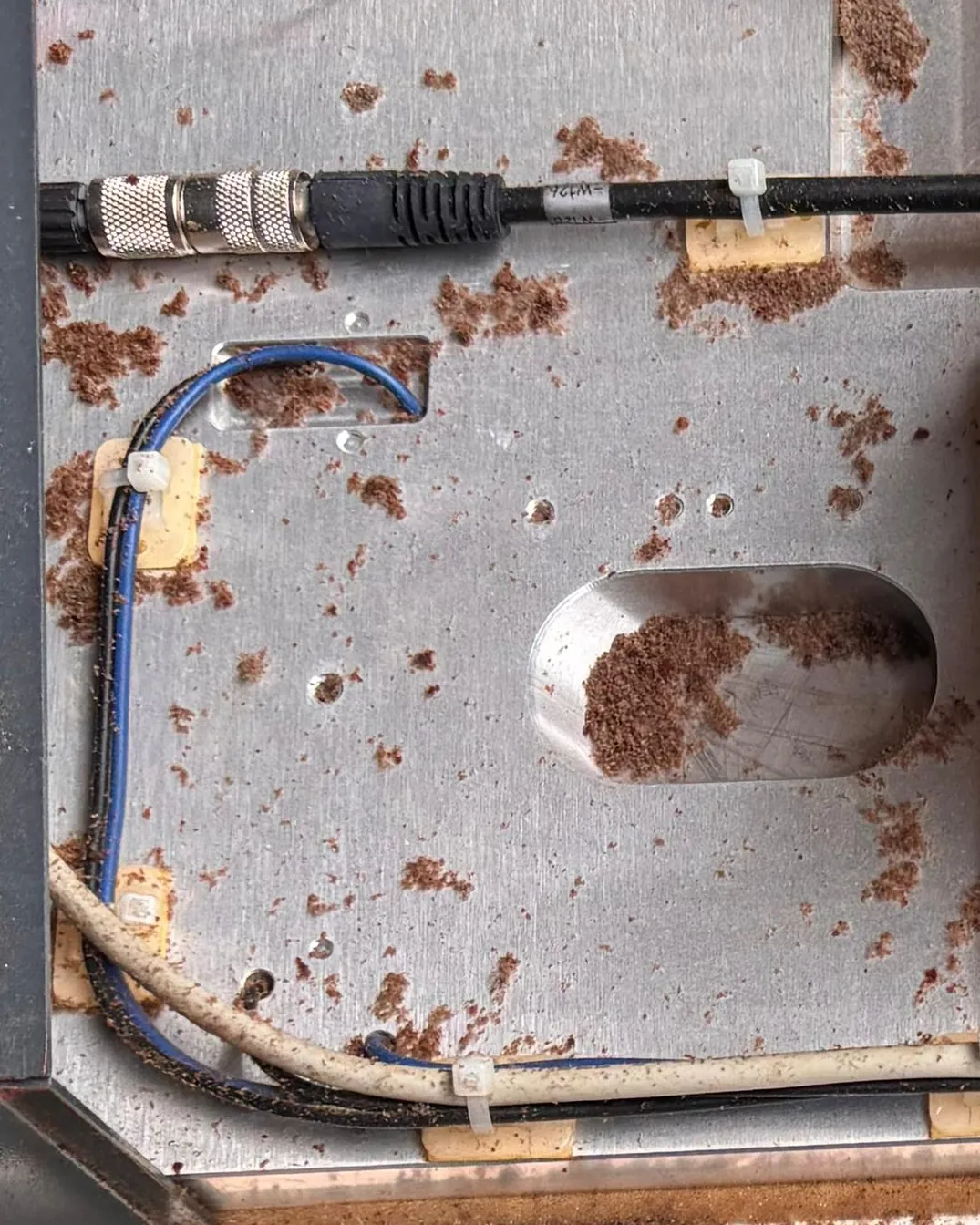 Grundplatte einer geöffneten Markierlaserquelle, übersät mit rotbraunen Rostpartikeln