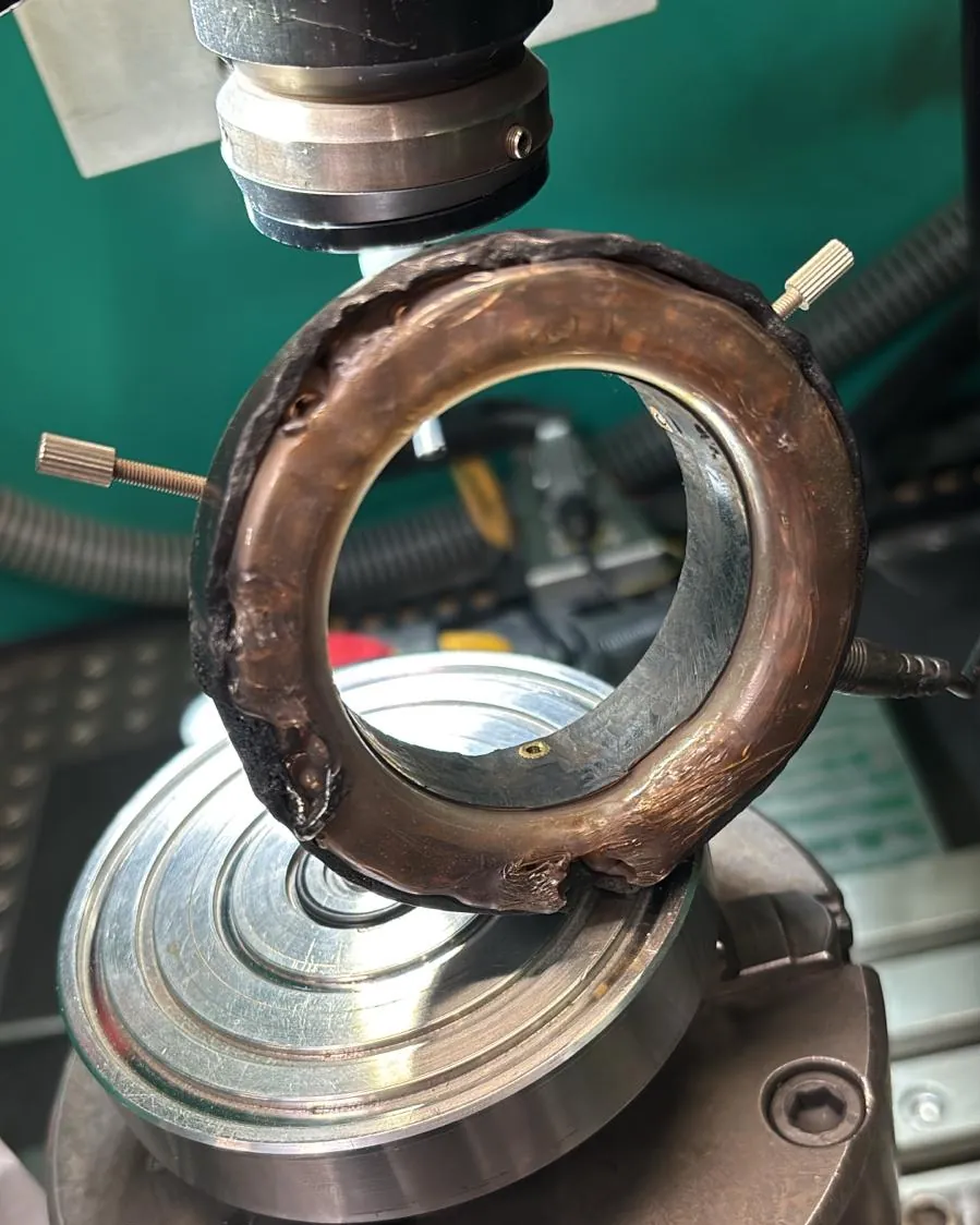Stark verbrannter, kupferfarbener Schutzring unter einem Laserkopf über einem Spannfutter