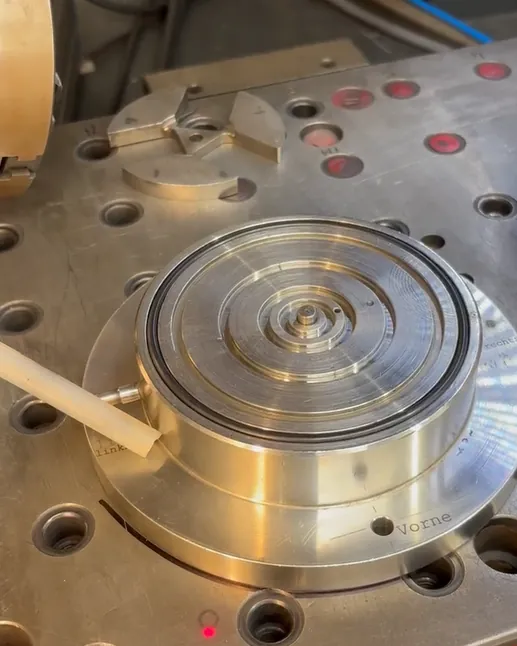 Rundes Spannfutter auf einem Aufspanntisch mit Bohrungen, davor ein roter Pilotlaserpunkt