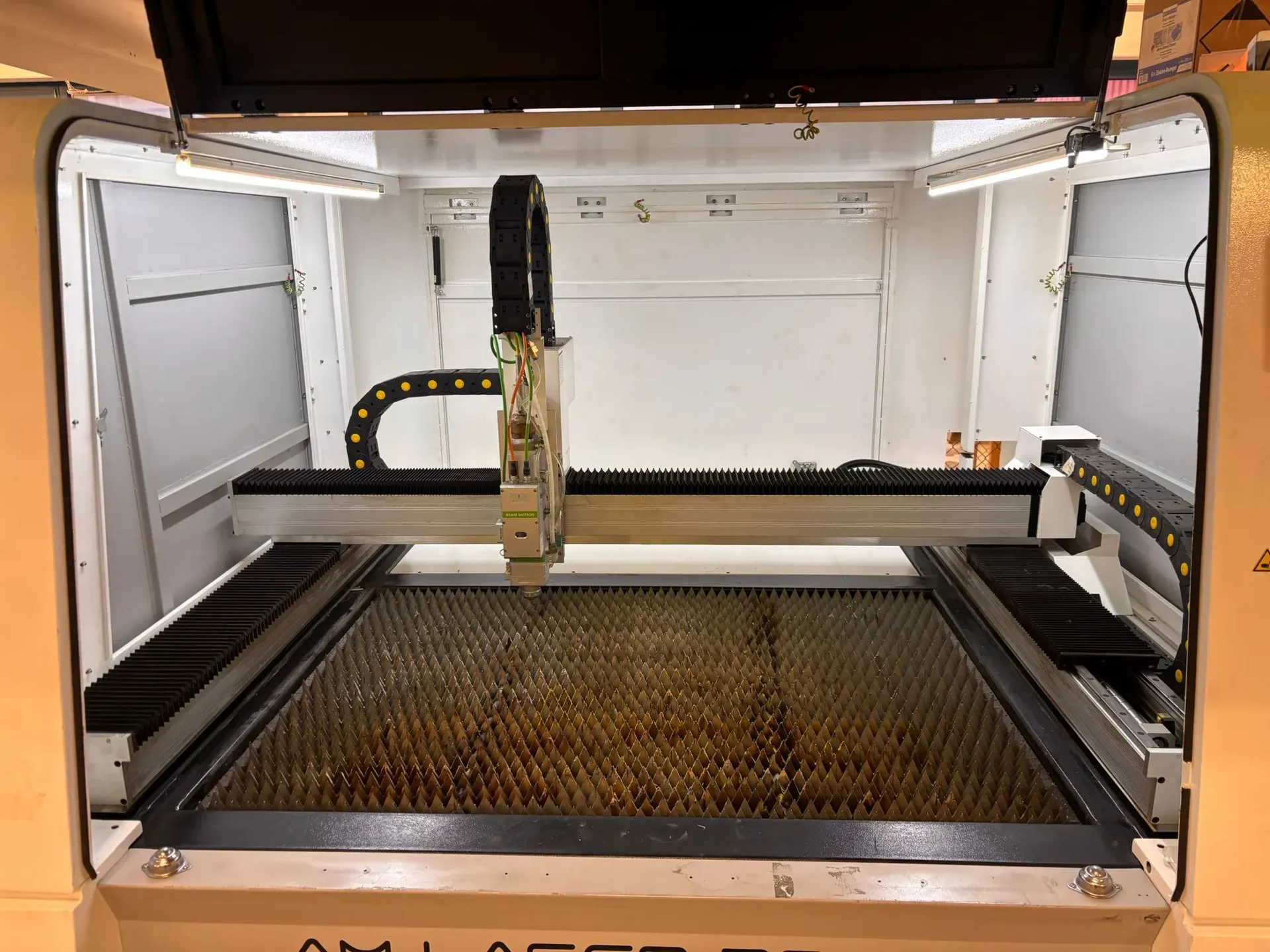 Geoeffnete Lasermaschine mit Portal und Schneidkopf ueber dem Wabentisch