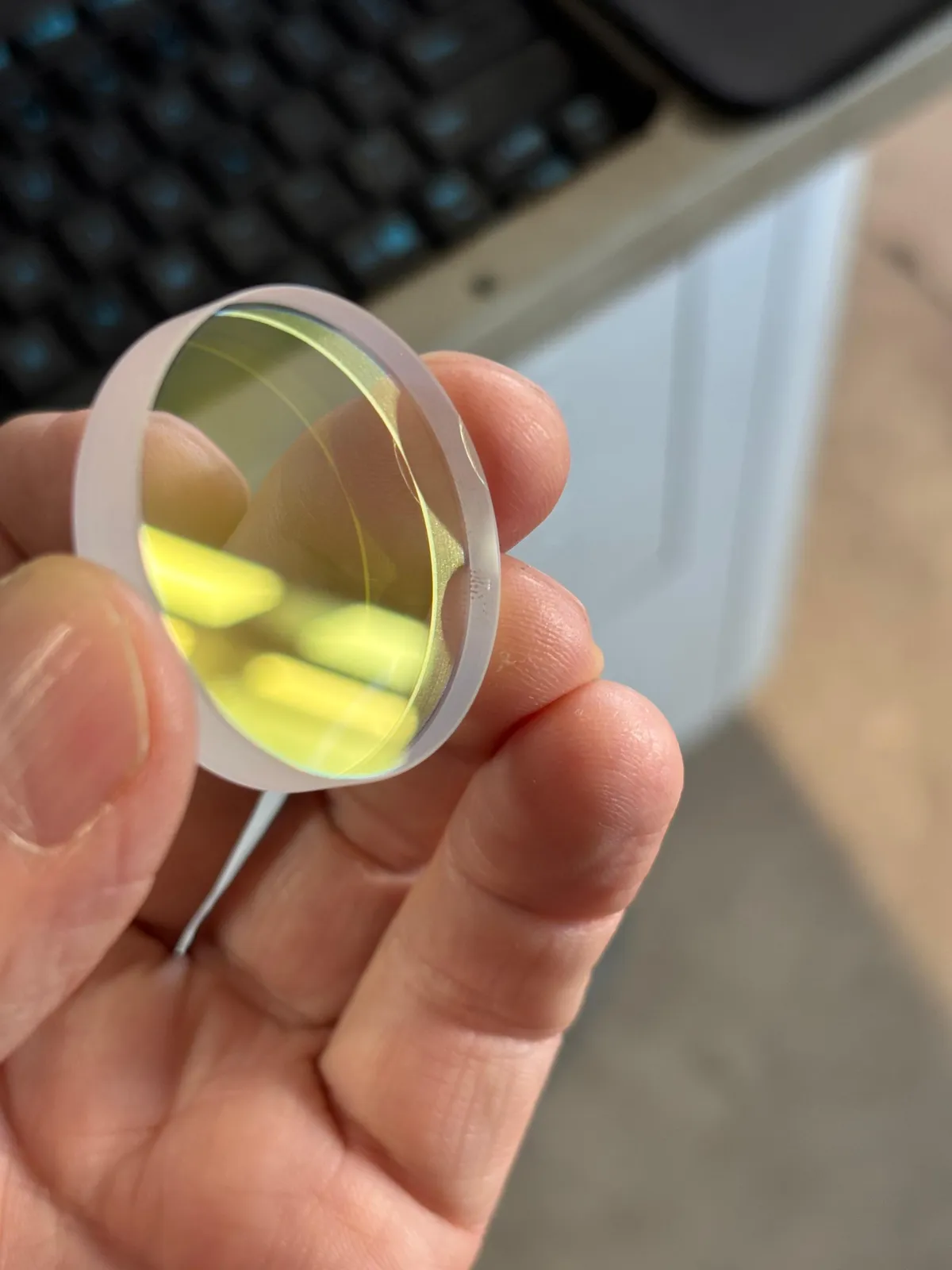 Laser-Optik gegen das Licht gehalten, Beschichtung im Streiflicht geprueft